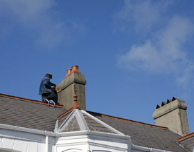 Worker repairing pitched roof with chimney